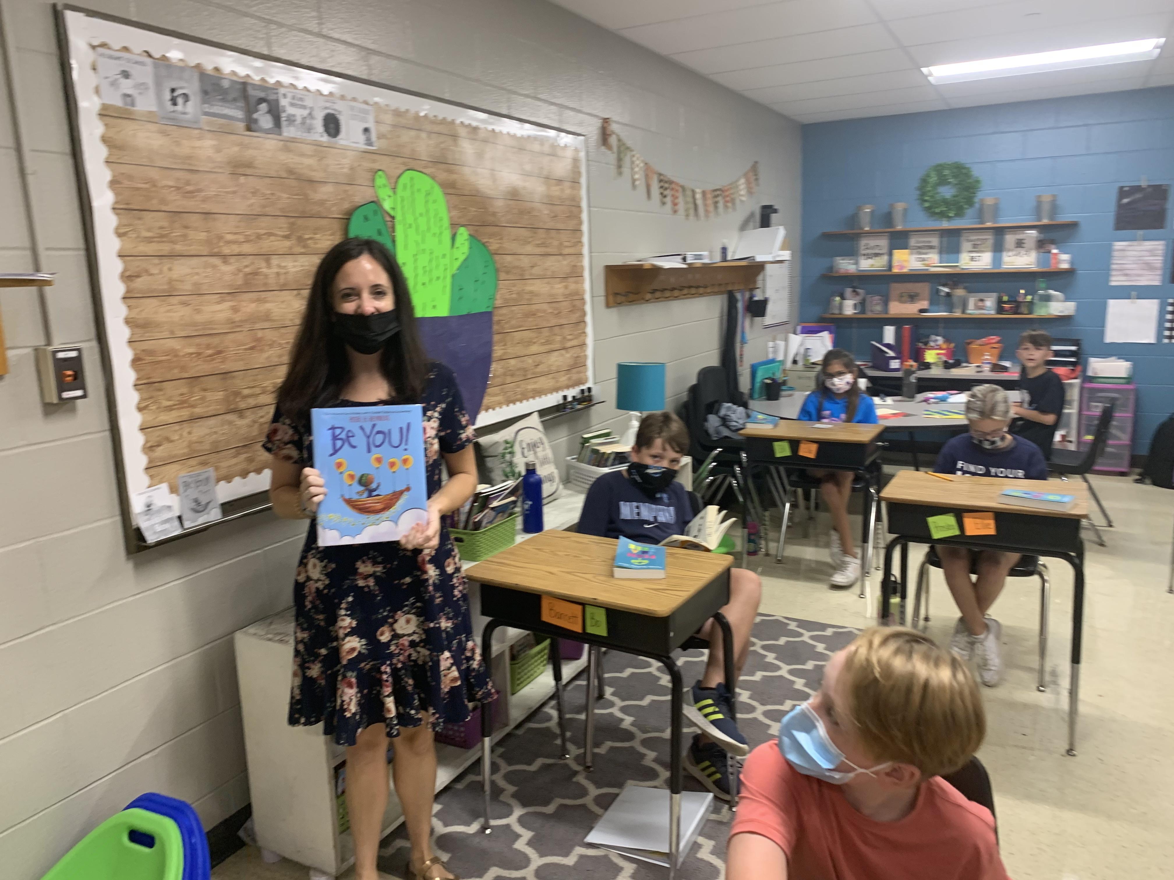 Elementary school teacher holds up book in front of class